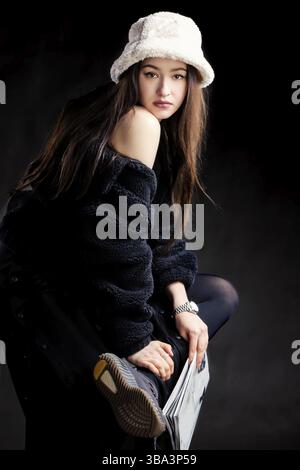 Beautiful stylish girl in dark clothes and a fashionable hat against a dark background Stock Photo