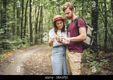 Young caucasian couple uses a smartphone to navigate in the forest. Hiking tourists orientation on the terrain using an online map, an application in Stock Photo