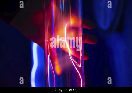 The hand touches a glass tube with red and blue light from the gas Stock Photo