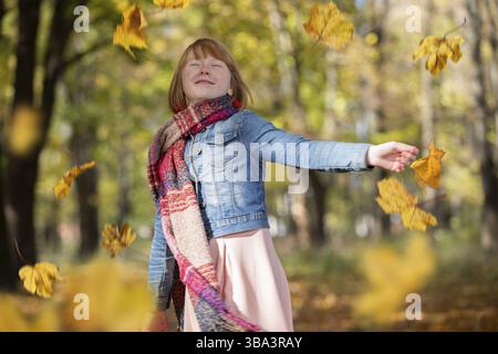 Happy red-haired girl scatters maple leaves in the autumn park Stock Photo