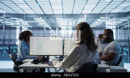 Admin arriving in server hub, sitting at computer desk, checking recovery plan, monitoring data center energy consumption across components, making sure sensors are functioning optimally, camera B Stock Photo