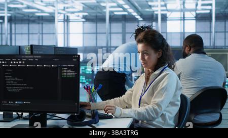 Upbeat computer scientist working in high tech server hub capable of processing vast amounts of data. Smiling woman at PC typing on keyboard, updating servers controlling network resources, camera A Stock Photo