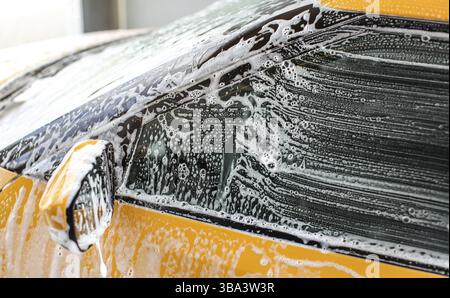 Side window and mirror of yellow car washed in carwash. Strokes from brush visible on glass in white shampoo and foam, Liptovsky Mikulas, Slovakia, Eu Stock Photo