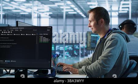 Man working in server hub capable of processing vast amounts of data. IT programmer at PC desk typing on keyboard, updating servers controlling network resources, camera A Stock Photo