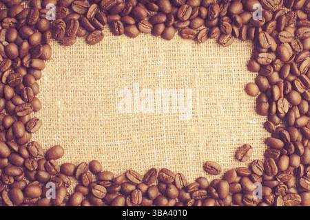 Spilled coffee beans frame over burlap textile Stock Photo