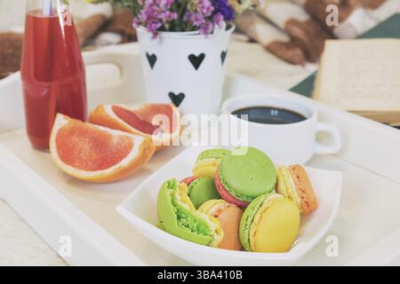 Breakfast in bed with hot coffee and macaroons. Healthy breakfast kept on bed with books and flowers Close up of a cup of coffee with cookies, fresh j Stock Photo