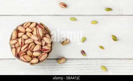 Tabletop view, small bowl with red Turkish pistachios, more nuts scattered on white board desk, Liptovsky Hradok, Slovakia, Europe Stock Photo