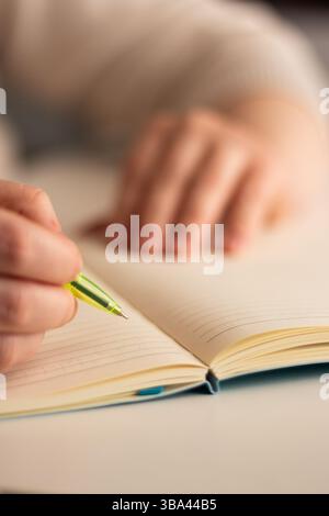 Close up image of human holding pen and writing something on blank white page in notebook Stock Photo