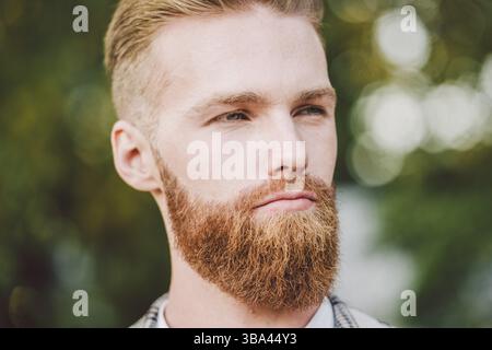 Portrait of Caucasian stylish bearded groom in vintage suit posing outdoors in sunny weather. Handsome man with beard in plaid jacket. Male model at w Stock Photo