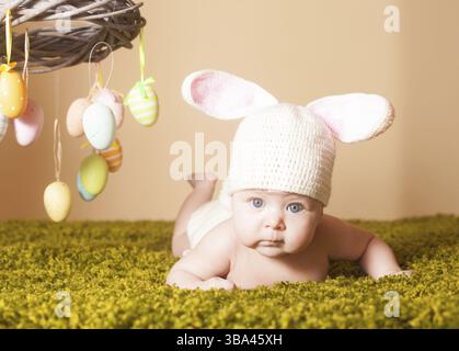 Three months baby lying on his stomach as a Easter bunny on the grass with eggs Stock Photo