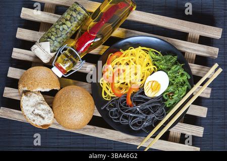 Hiyashi wakame with sesame and nut sauce, black and corn noodles, boiled egg. Bottle of olive oil with chili pepper, black olives and capers in jar, b Stock Photo