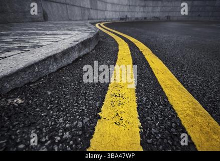 Detail of curved double yellow line on black asphalt painted along curb Stock Photo