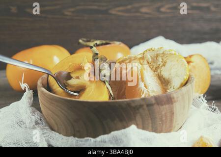 Fresh persimmons and tangerines fruits in bowl on dark wooden background. Coloring and processing photo Stock Photo