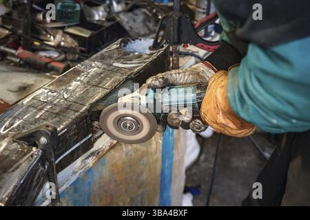 Man working with rotary angle grinder at workshop, closeup detail to hands holding the tool Stock Photo