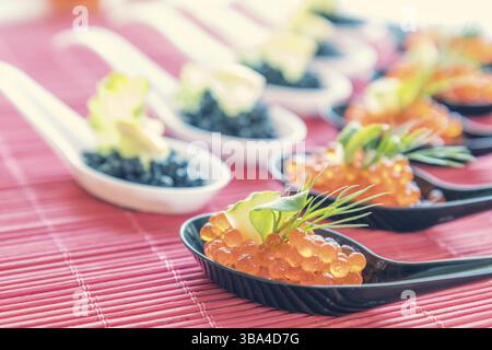 Delicious red and black caviar fish close-up in white and black spoons on white table. Beautifully decorated catering banquet table Stock Photo