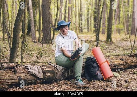 Young woman having trouble feeling knee pain during travel in forest. Injury on way to camp. female tourist got leg injury in forest and gets hurt. He Stock Photo