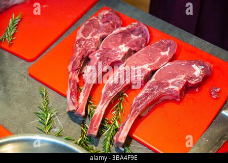 Four raw tomahawk steaks arranged on a red cutting board with sprigs of fresh rosemary, ready for cooking or grilling. Stock Photo