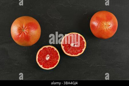 Pink grapefruits, one cut in half on black slate board, top view, Liptovsky Hradok, Slovakia, Europe Stock Photo