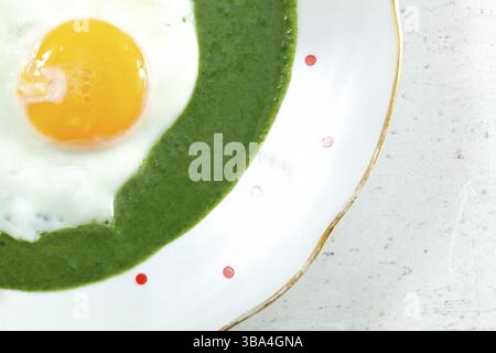 Flat lay close up photo, sunny side up made egg in spinach on white plate with small red dots, Liptovsky Hradok, Slovakia, Europe Stock Photo