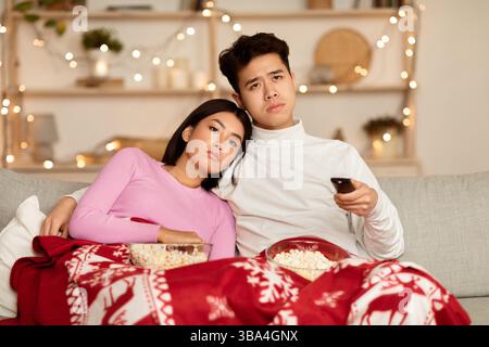 Bored Asian Couple Watching TV Celebrating Christmas At Home Stock Photo