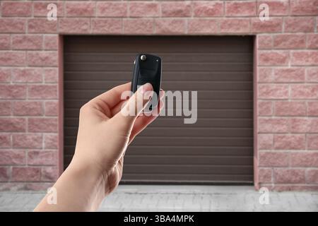 Woman using remote to control garage door outdoors, closeup Stock Photo