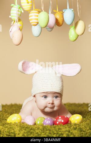 Three months baby lying on his stomach as a Easter bunny on the grass with eggs Stock Photo