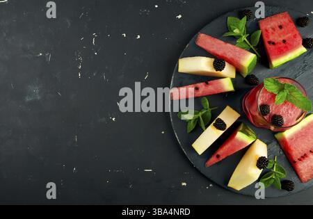 MELON WATERMELON BLACKBERRIES MINT AND A GLASS OF JUICE ON ROUND WOODEN BACKGROUND. RIPE WATERMELON JUICY MELON BLACKBERRY MINT COCKTAILS ON A DARK WO Stock Photo