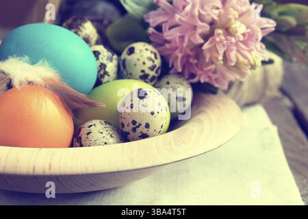 Easter colorful and quail eggs in wooden pot with pink hyacinth on dark wooden table. Toned photo Stock Photo
