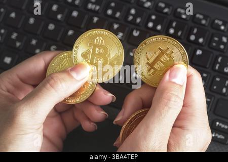 Woman hand holding golden coloured bitcoin coins over black laptop keyboard, Liptovsky Mikulas, Slovakia, Europe Stock Photo