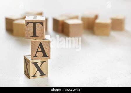 Three wooden cubes with word TAX on white table, more in background, space for text in right down corner, Liptovsky Hradok, Slovakia, Europe Stock Photo