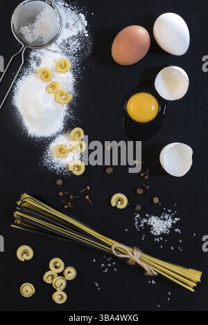 Traditional and black uncooked Italian pasta Linguine, Italian pasta Cappelletti with white and brown chicken eggs, broken white egg, flour, metal sie Stock Photo