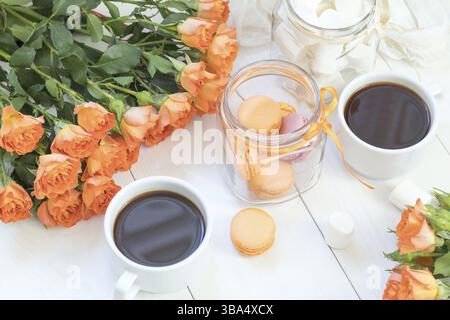 Orange mango macaroons, cup of coffee, marshmallow and fresh little roses on light wooden background. Sunlight. Coloring and processing photo with lig Stock Photo