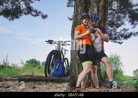 Happy couple searching on map in smartphone destination. man and woman in helmets traveling mountain biking over rough terrain. Theme tourism and navi Stock Photo