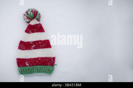 Knitted Christmas hat on a white background. Funny Christmas hat on snow background Stock Photo