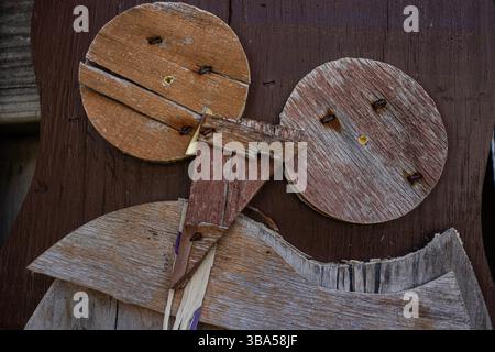 Shabby brown owl decoration made with wood cutouts hangs on a wooden fence. The decoration is falling apart, old and splintering, with peeling paint. Stock Photo