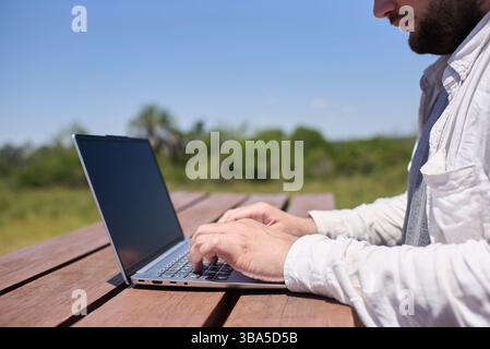 Unrecognizable man working on his laptop at an outdoor table on a sunny day. Concept: digital nomad working remotely while traveling enjoying a lifest Stock Photo
