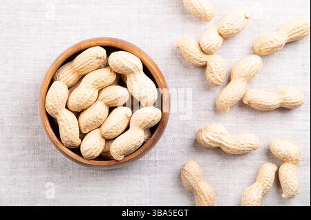 In-shell roasted peanuts in a wooden bowl on linen. Whole, crunchy nut, fruit of Arachis hypogaea encased in its natural shell. Stock Photo