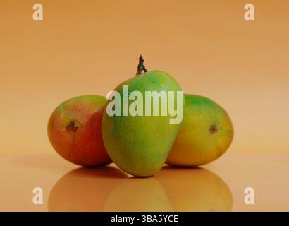 Fresh ripe mangoes resting on a bed of dry hay against a warm orange background. Organic tropical fruit display ideal for summer. Stock Photo