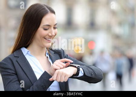 Happy executive standing in the street checking smartwatch Stock Photo