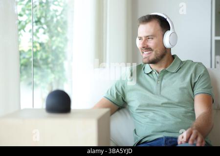 Happy man listening music from smart speaker using headphone sitting on a couch at home Stock Photo