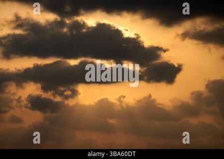 Golden sunset sky with dramatic dark clouds and rays of sunlight streaming through a breathtaking natural scene. Stock Photo