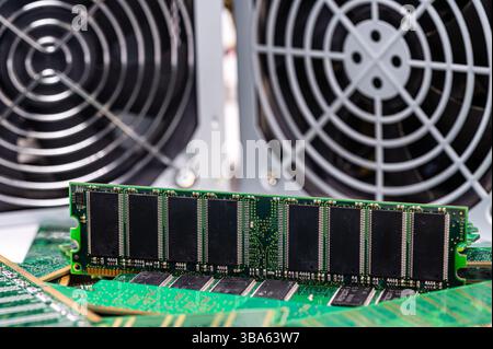 RAM modules placed on a circuit board beside large cooling fans in a tech workspace. Stock Photo