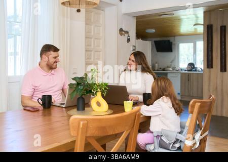 Latin family using laptops and enjoying breakfast together at the dining room table, working and studying from home Stock Photo