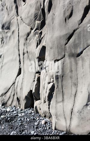Smooth weathered basalt cliff with dark pebble shore Stock Photo
