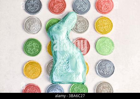 Foil-wrapped chocolate bunny surrounded by colorful Easter coins Stock Photo
