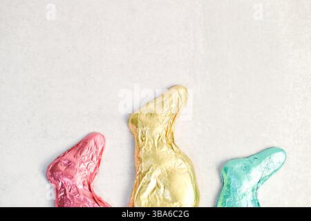 Foil-wrapped chocolate Easter bunnies in pastel colors on white. Stock Photo