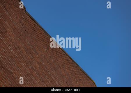 Diagonal red brick wall with blue sky forming geometric pattern Stock Photo
