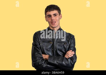 Portrait of confident young man crossing his arms, wearing black leather jacket on yellow background Stock Photo