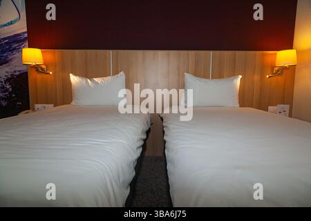 A hotel room with two beds, lit by the soft light of a lamp standing on the bedside tables. Stock Photo