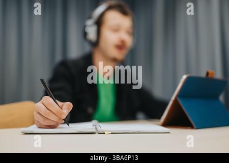 Teenager Studying While Using a Tablet and Taking Notes In a Journal Stock Photo